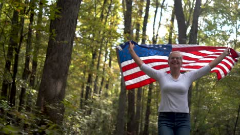 pretty blonde woman running through a forest with a flag flying behind her with the sun sparking through the trees