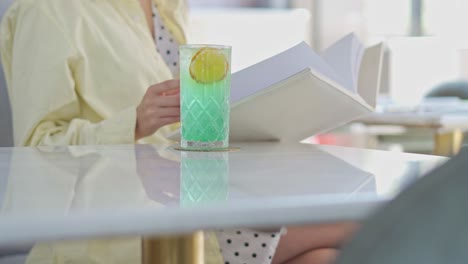 A-woman-siting-on-a-table-in-the-living-room-with-her-book-and-drink,-close-up-shot