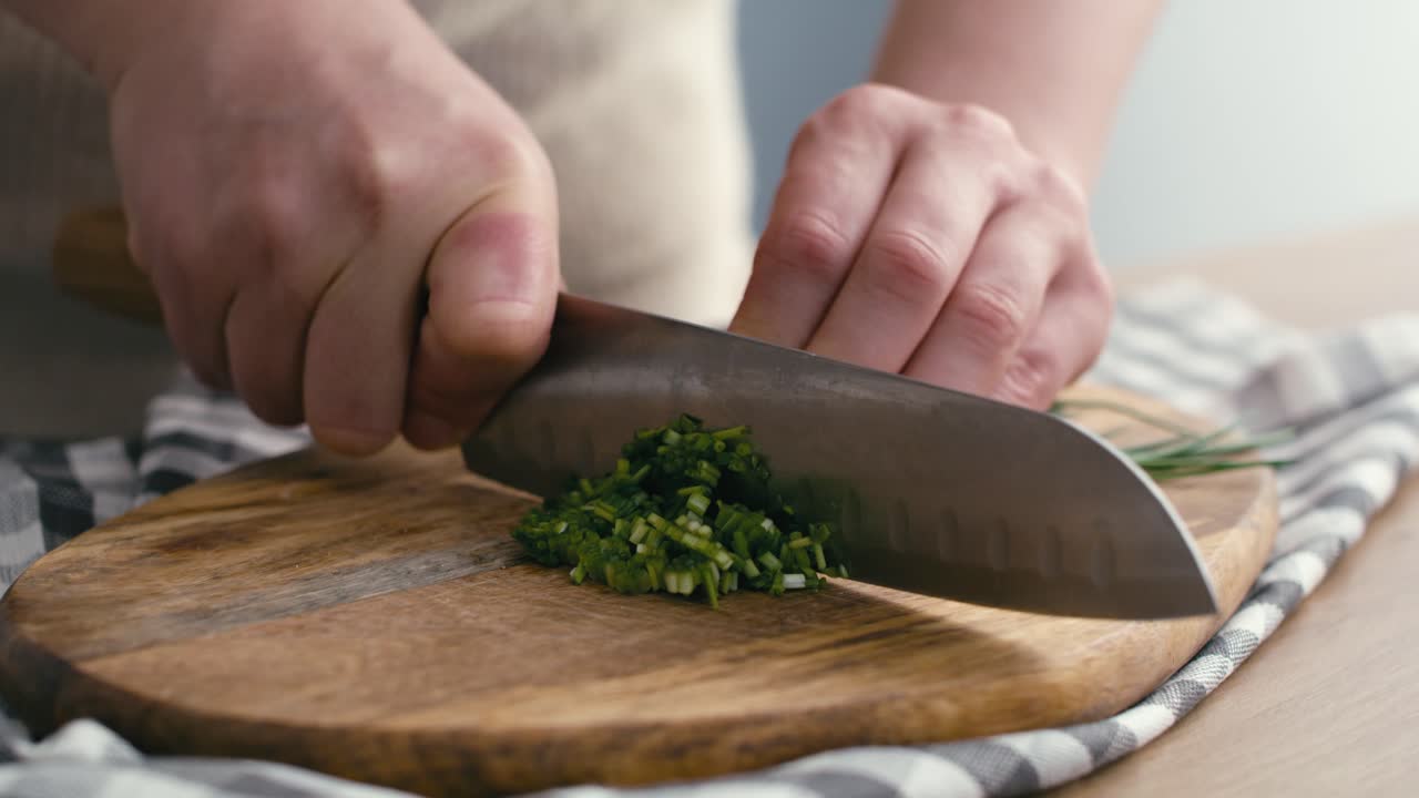 Close up of hands of woman cutting chives at the kitchen.