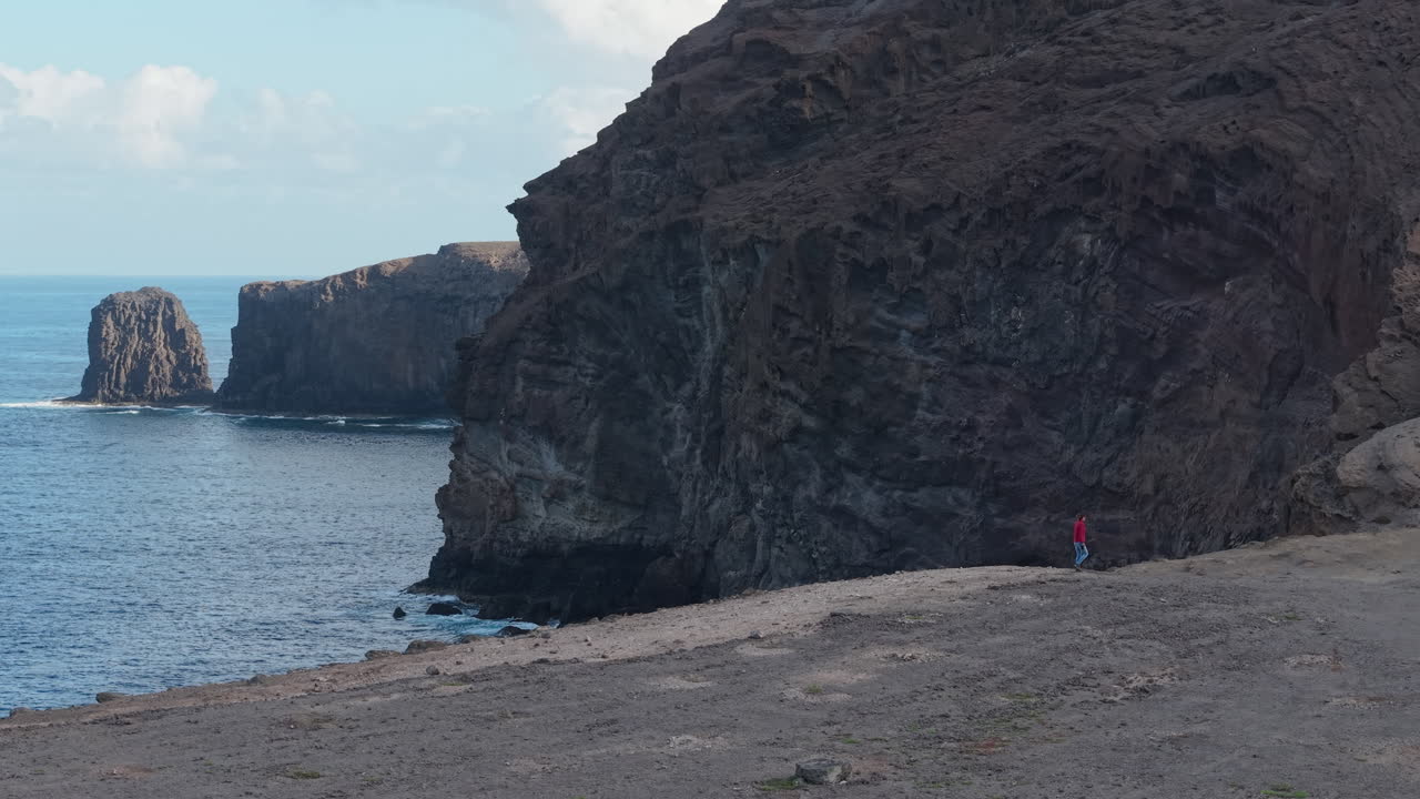 Lone hiker walking on a dramatic coastal cliff path near the atlantic ocean in Canary Islands