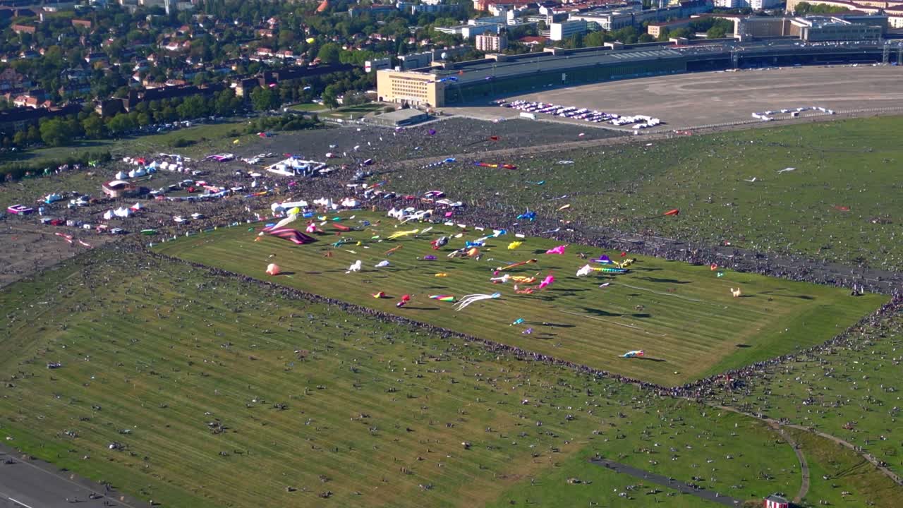 Large crowd of people gathering at the Tempelhofer Feld giant kite festival in Berlin, Germany. Fantastic aerial view flight fly push forward drone camera pointing down