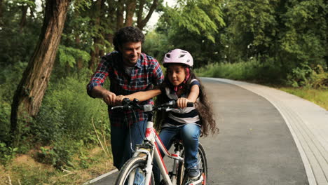 closeup. portrait of a little girl and her father. dad teaching his daughter to ride a bike. he lets her go. moving camera. blurred background