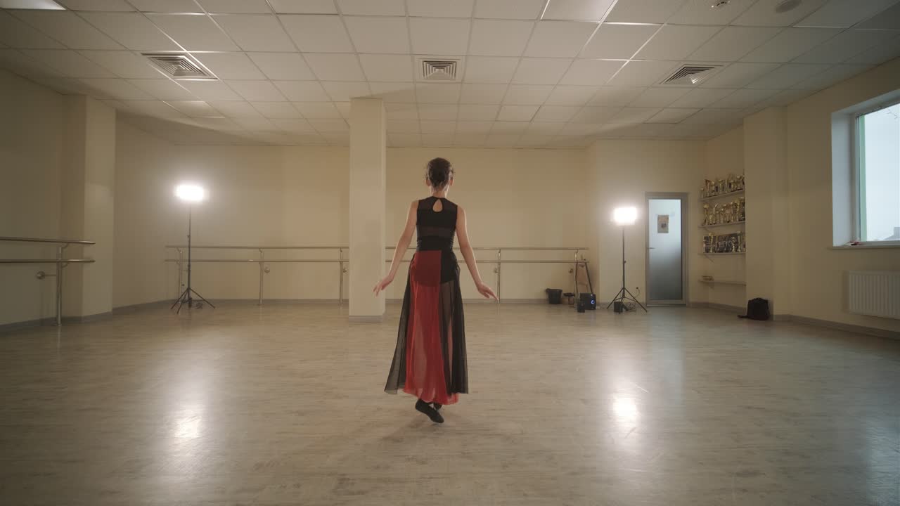A group of young ballet students in black dancewear practicing positions in a spacious ballet studio with wooden flooring and wall-mounted barres. Focused expressions and synchronized movements.