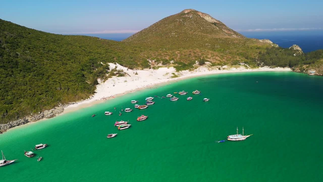 브라질 리우데자네이루 주 아라야르 도 카보 해변에서 보트와 세일보트와 함께 푸르키즈색 바물과 함께 식물과 해안의 언덕을 볼 수 있습니다.