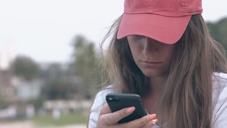 Gebräunte-Dame-Mit-Leuchtend-Roter-Mütze-Sitzt-Mit-Schwarzem-Telefon