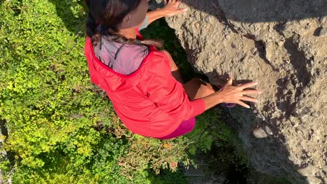 Vertical-video-of-sporty-older-woman-climbing-up-rocks