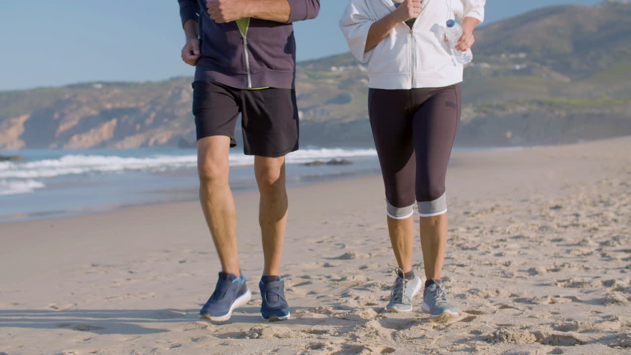 pareja de ancianos en ropa deportiva corriendo juntos en una playa de arena
