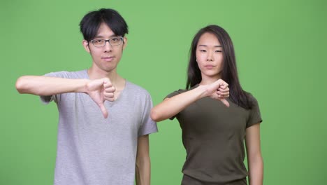 young asian couple giving thumbs down together