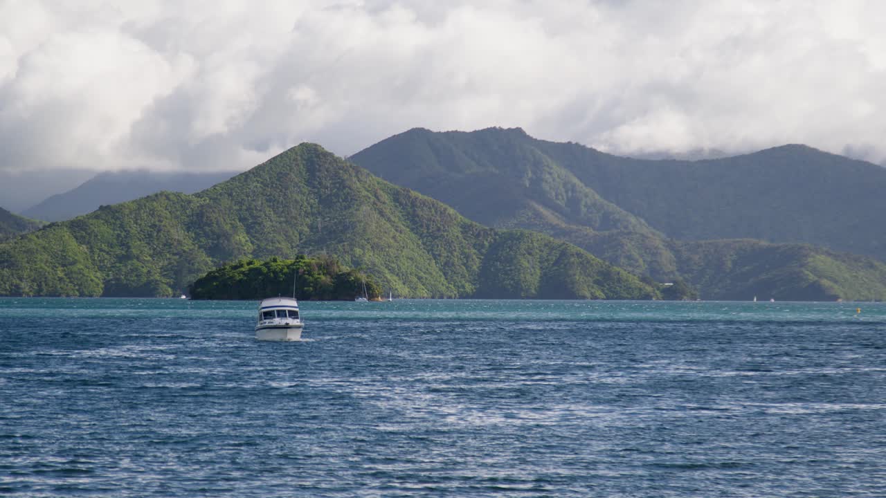 A boat slowly floating towards the camera through the Marlborough Sounds in the South Island of New Zealand with Mabel island in the background