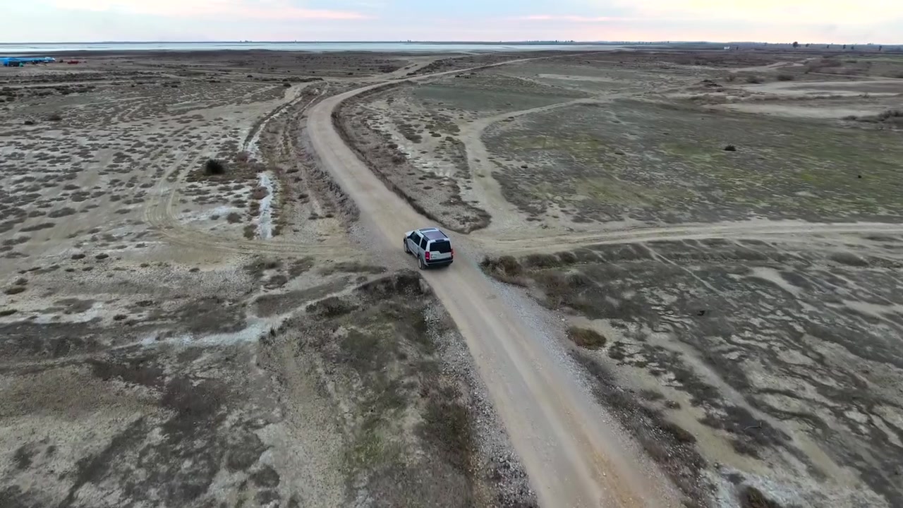 SUV argentato che percorre una strada sterrata remota in un vasto paesaggio