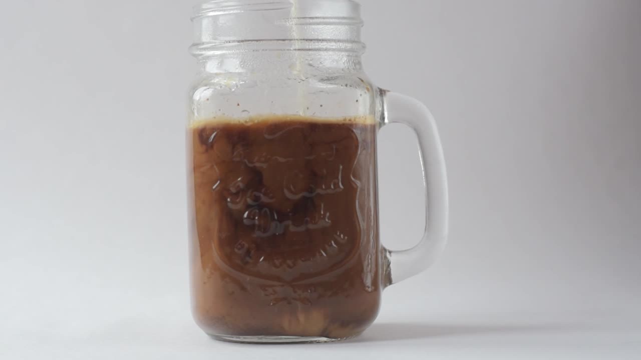 Caffè nero che si mescola con il latte in una tazza di vetro