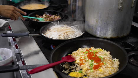 Cinematic-shot-of-pan-after-pan-crowding-working-professional-restaurant-kitchen,-chef-sautes-vegetables-in-pan-along-side-a-variety-of-other-simmering-dishes,-slow-motion-slider-4K