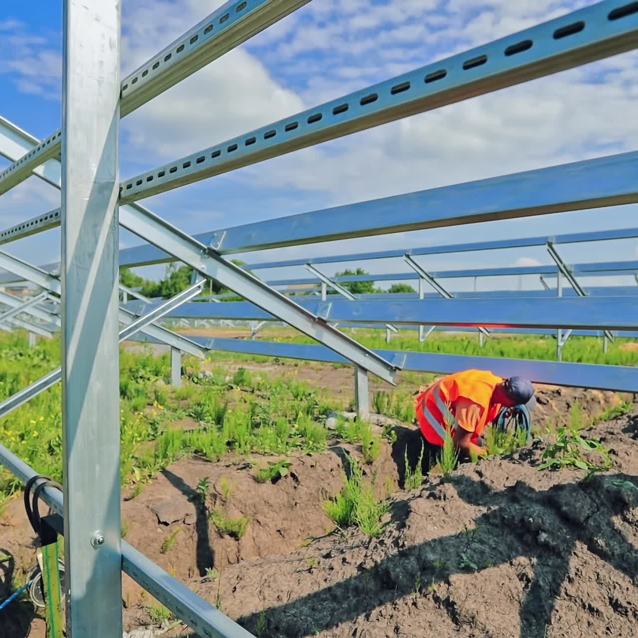Building of an innovative solar power plant. Worker installing wires into the ground on the new solar farm in a bright summer day.