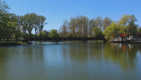 Parte-Superior-De-La-Vista-De-Drones-De-Agua-Con-Movimiento-Hacia-Adelante-Desde-Un-Lago-Natural-Y-Un-Puente-Ubicado