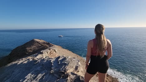 mujer joven observa las maravillosas vistas ubicadas cerca de la playa de medio almud y donde un barco navega en el horizonte