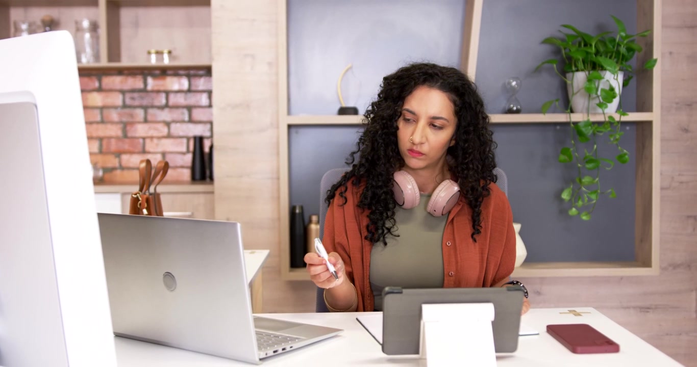 African American woman at home office seeing tablet cable reaching using stylus working on laptop