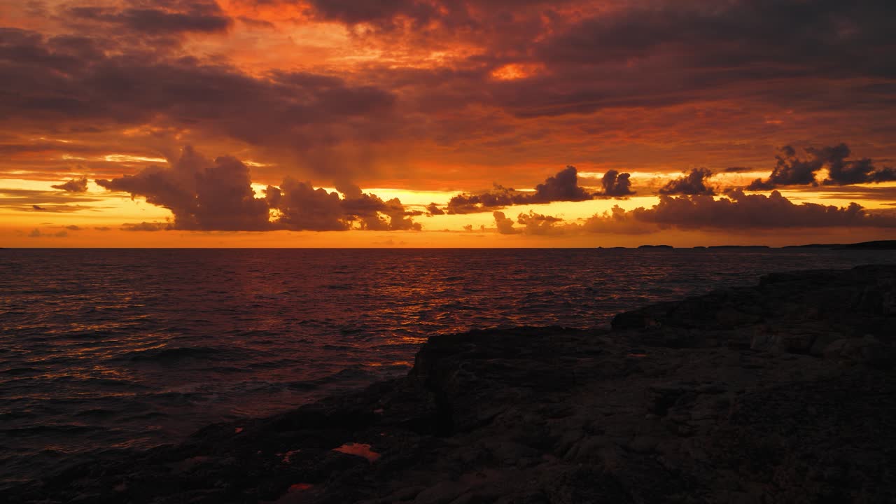 Red and orange clouds reflecting in dark sea water during sunset in Istria, Croatia