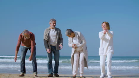 excited senior men and women standing on beach and jumping