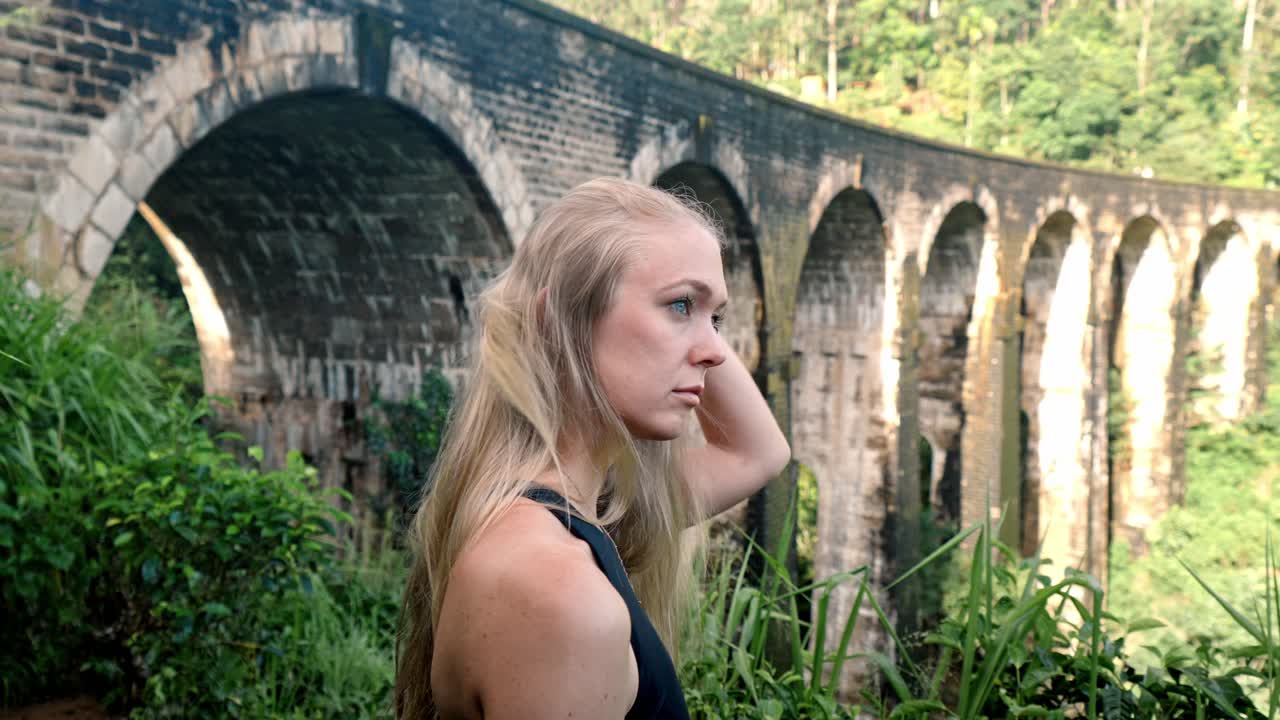 A young woman observes the historic Nine Arch Bridge from a nearby hillside in Ella, Sri Lanka.