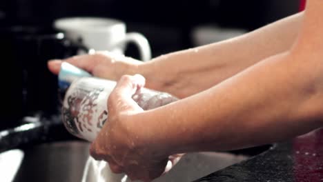 woman's hands washing glass cup with sponge and soap in kitchen sink at home, slow motion