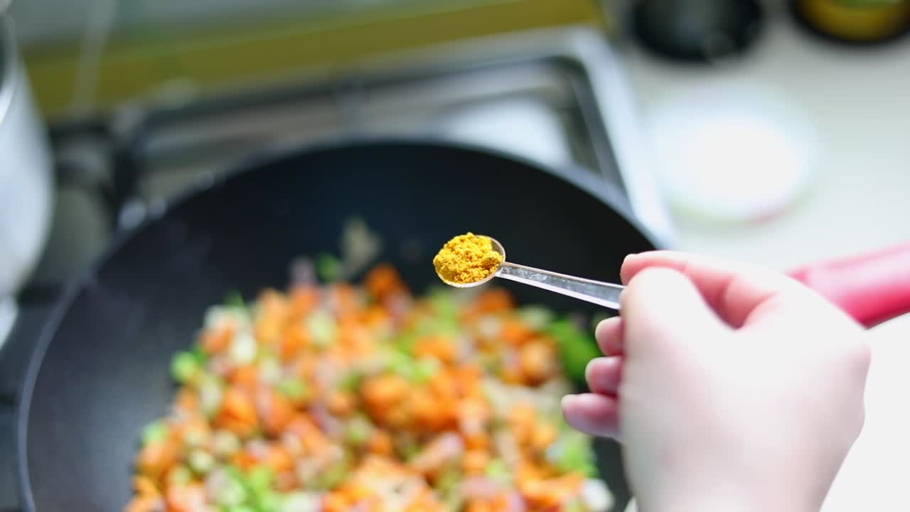 rociando una cucharadita de polvo de cúrcuma en la cocina de alimentos en la sartén