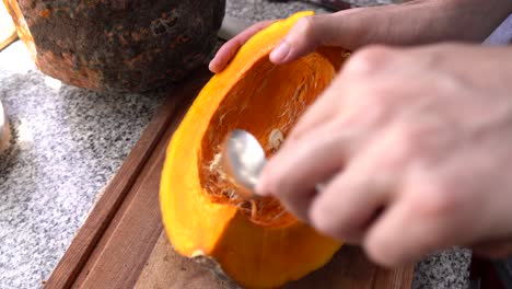 removing pumpkin pulp and seeds with a spoon in the kitchen