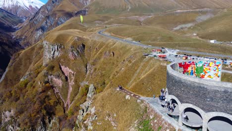 Paraglider-flying-against-the-background-of-the-beautiful-Caucasus-mountains-near-the-monument,-Georgia