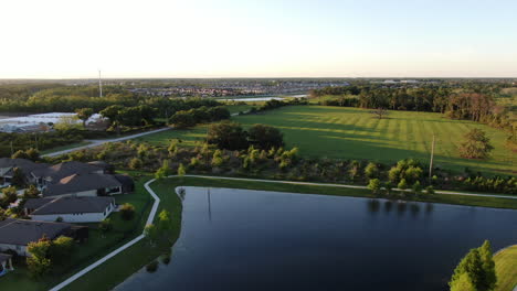 Panorámica-Sobre-Un-Lago,-Casas-Y-Una-Granja-Con-Vacas-Durante-Un-Atardecer-De-Primavera