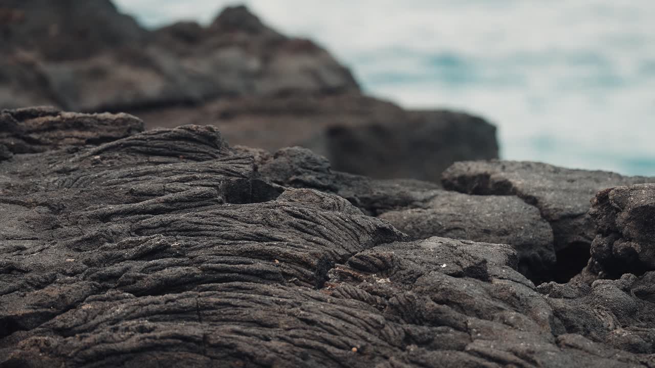 Layered dark black volcanic rock with ocean waves crashing in background, static backdrop