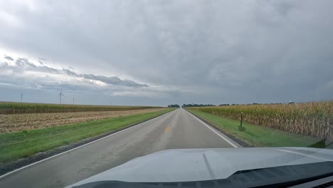 - pov conduciendo en un camino rural pasando por granjas y campos de maíz que pronto serán cosechados en un día nublado