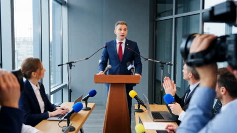 man speaking at a press conference with journalists present