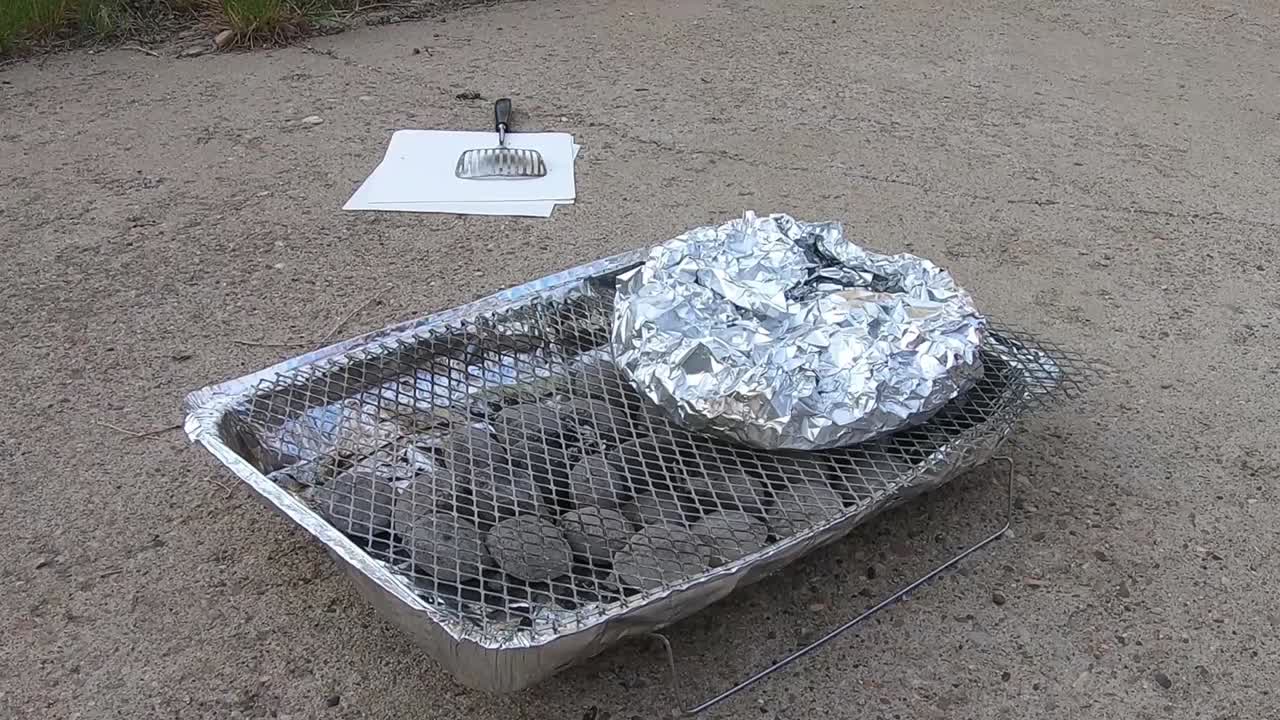 Potatos in aluminum tin foil on a throw away BBQ sitting in a driveway on a sunny day.