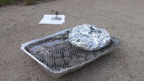potatos in aluminum tin foil on a throw away bbq sitting in a driveway on a sunny day.