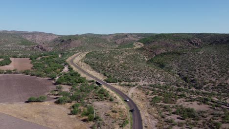 Road-with-two-cars-in-front-shot-with-a-drone-and-mountains-in-the-background