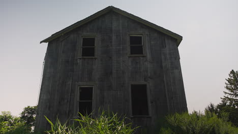 Frontal-view-of-windows-on-eerie-creepy-abandoned-wooden-home-in-field