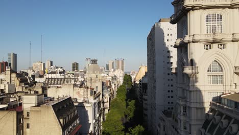 Carretilla-Aérea-Revelando-La-Torre-Del-Palacio-Barolo-En-La-Avenida-De-Mayo-Con-árboles-Rodeados-De-Edificios-De-Buenos-Aires-Al-Atardecer