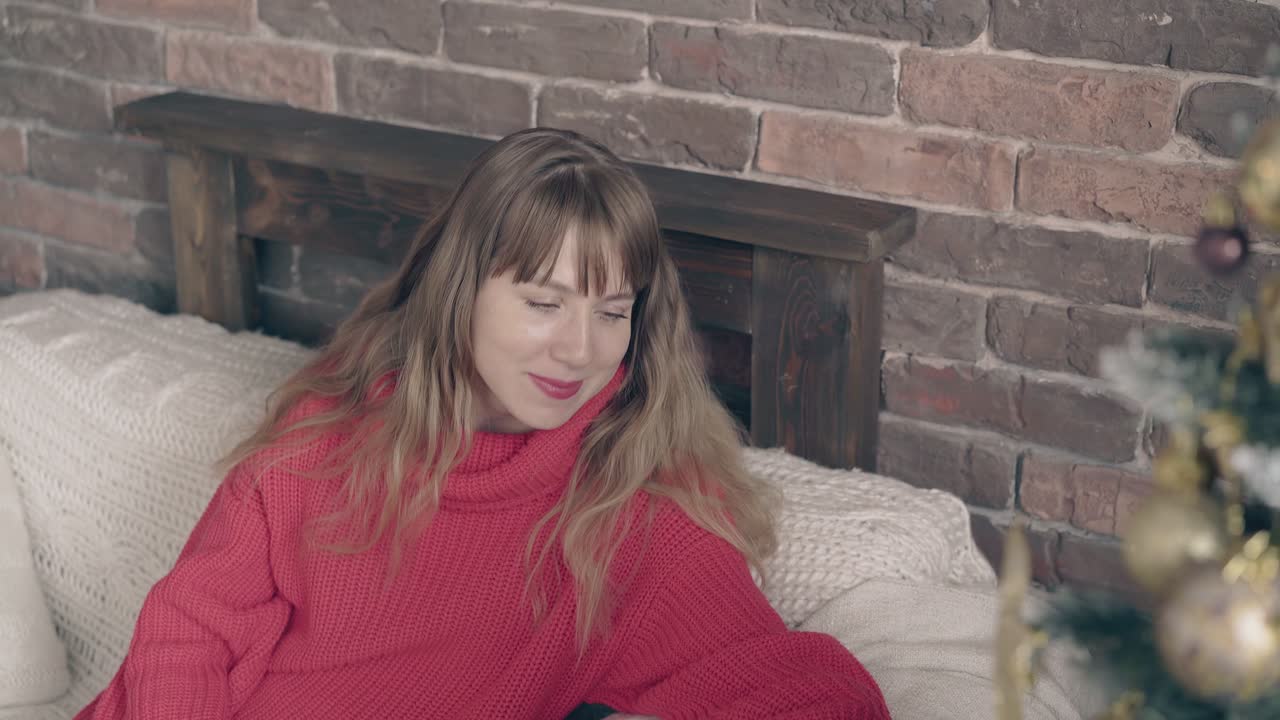 симпатичная женщина смотрит на елочные украшения с дивана