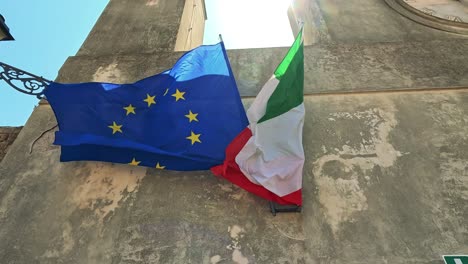 european and italian flags waving in sunlight