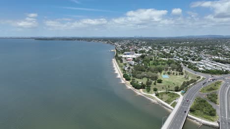 Drone-establishing-pull-away-shot-of-Ted-Smout-Memorial-Bridge-and-Brighton-Suburb,-camera-flying-over-water-Moreton-Bay-with-Brisbane-City-in-background