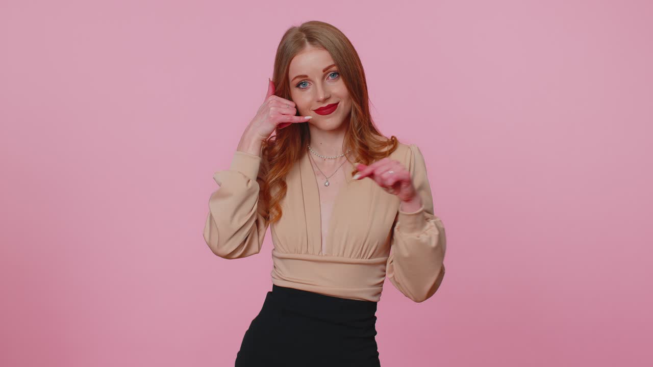 베이지 블라우스를 입은 유쾌한 소녀가 카메라를 바라보며 전화 제스처를 하고 있습니다.