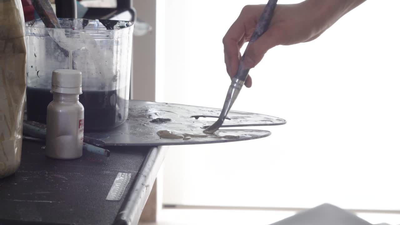 artista mezclando colores en paleta contra fuente de luz blanca, vista estática