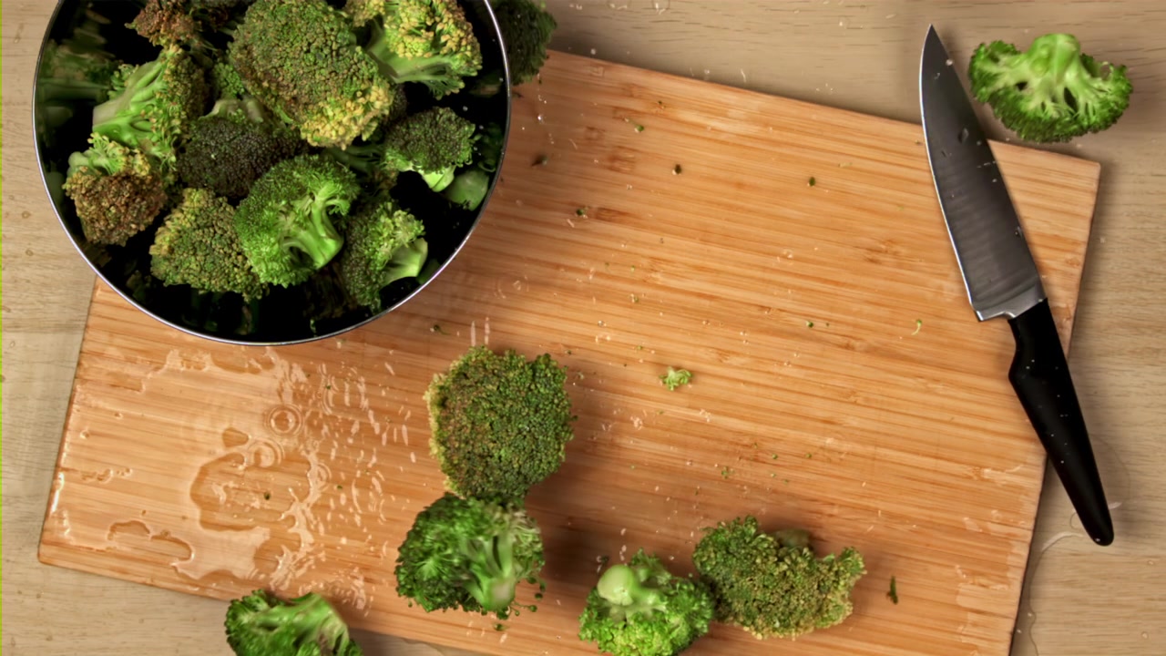 Cimette di broccoli freschi che cadono su un tagliere di legno