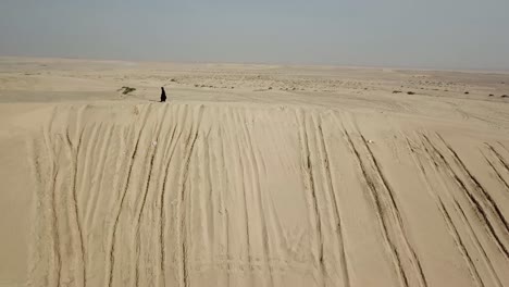 mujer caminando sobre una duna de arena con abaya negra