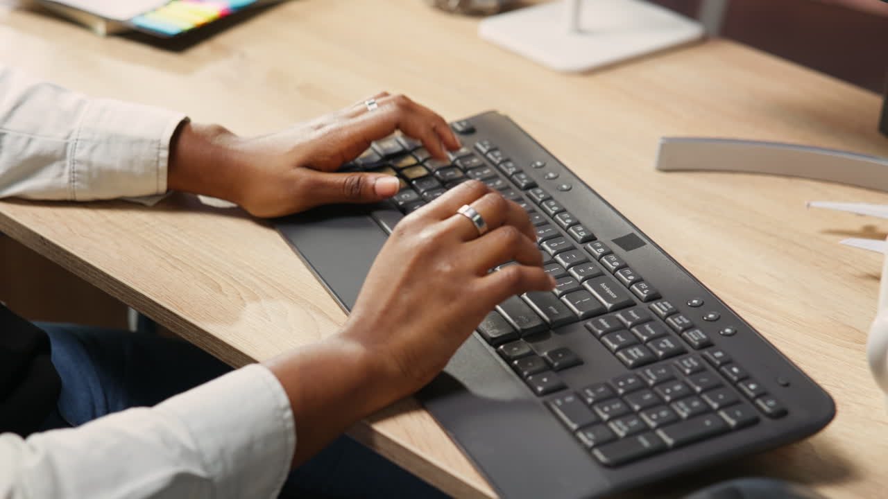 Person at home office desk typing on PC keyboard next to coffee mug, close up