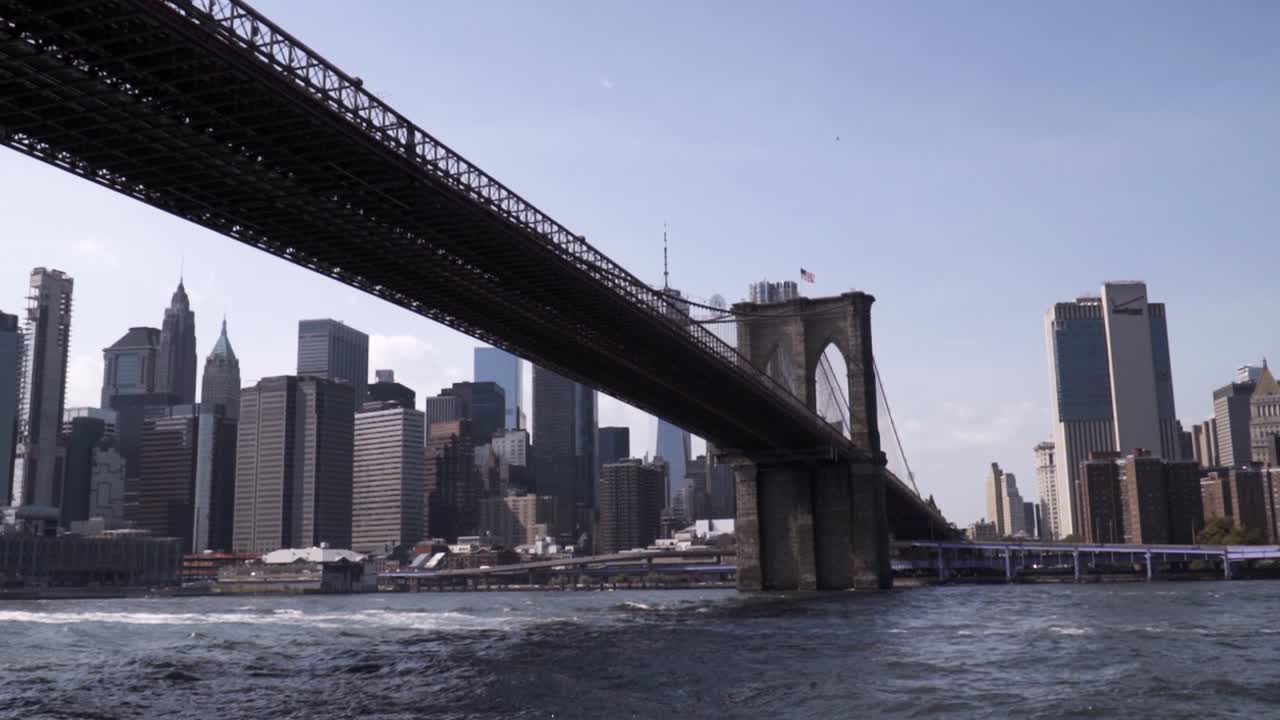 Iconic New York City Brooklyn Bridge with Manhattan in the background during sunny weather. Slow motion view from the East River- sightseeing boat.