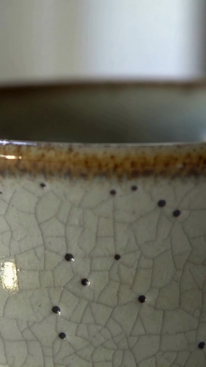 Vertical video: Sliding camera revealing ceramic cup rim on table to show crackle glaze, black dots
