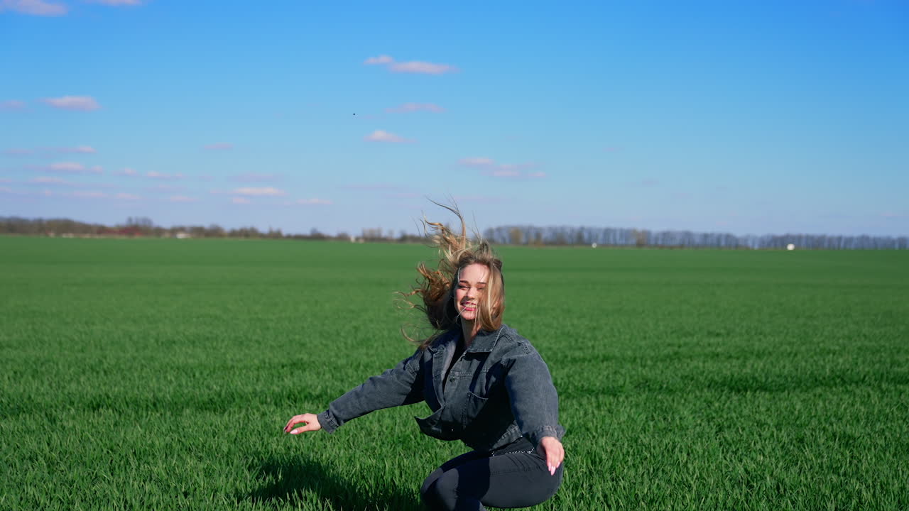 Happy girl in jeans on a green meadow. Beautiful young woman jumping joyfully on a field in a bright day. Cheerful model among nature.