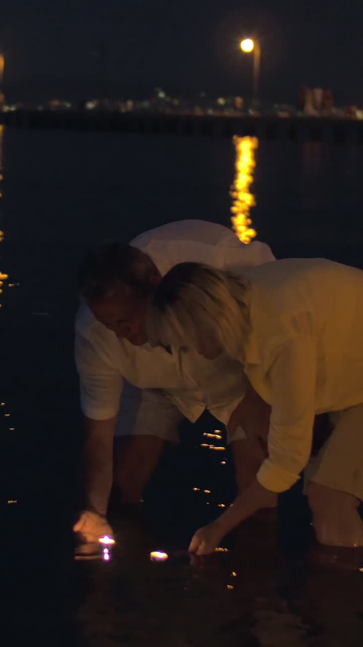 A couple releases wish lanterns into the ocean at night