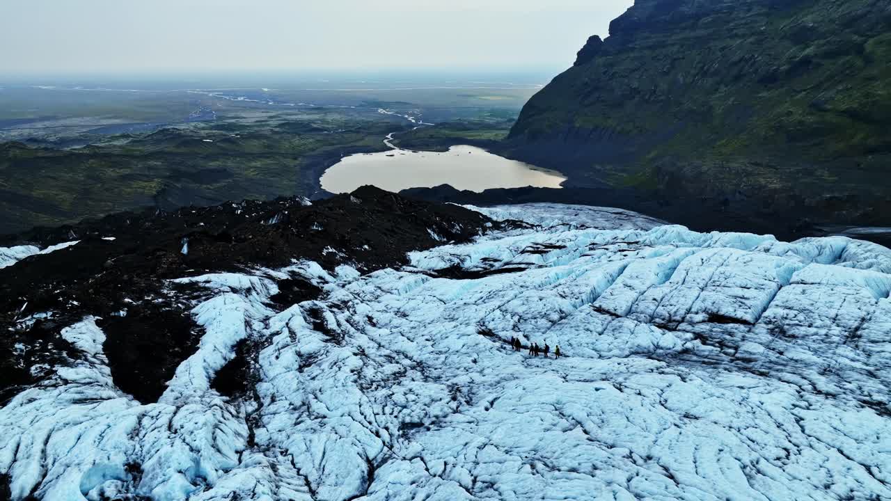 Cinematic aerial shot of an Icelandic glacier descending toward a distant lake and mossy plains, revealing rugged ice textures, dark volcanic ridges, and dramatic mountain terrain