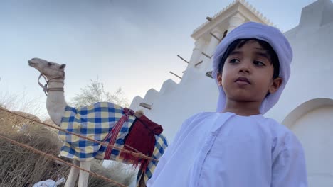 happy smiling emirati child looking at camel in traditional background